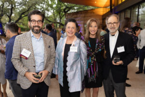Two men with drinks in their hands and two women standing in front of crowd at reception.
