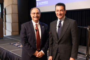 Description: Two men in dark suits stand in front of stage after presentation. Context: Larry Schlesinger with Scott Gottlieb.