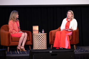 Two women wearing bright red clothing sit on stage together