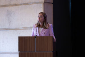 Description: Woman in pink suit addresses audience from podium. Context: GHS 2025 closing address