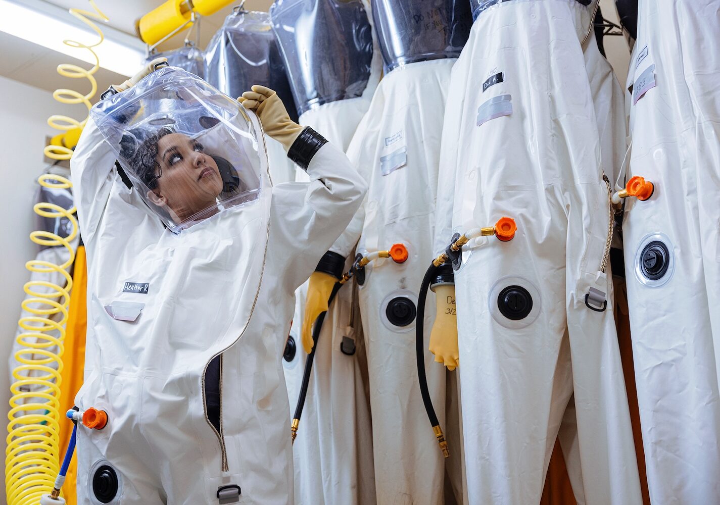 woman putting on white biosafety suit that covers entire body.