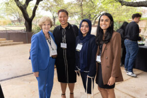 Older woman in blue pantsuit stands smiling with three younger women of color in professional clothes.