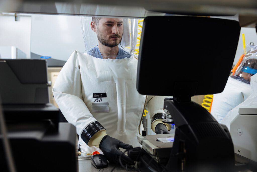 young man working at computer in full body biosafety suit.