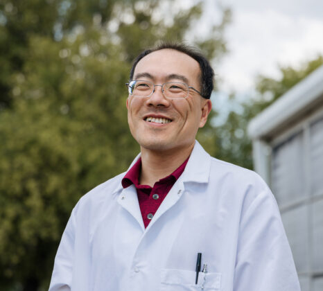 Image of Anthony Wang wearing a lab coat, outside, smiling.